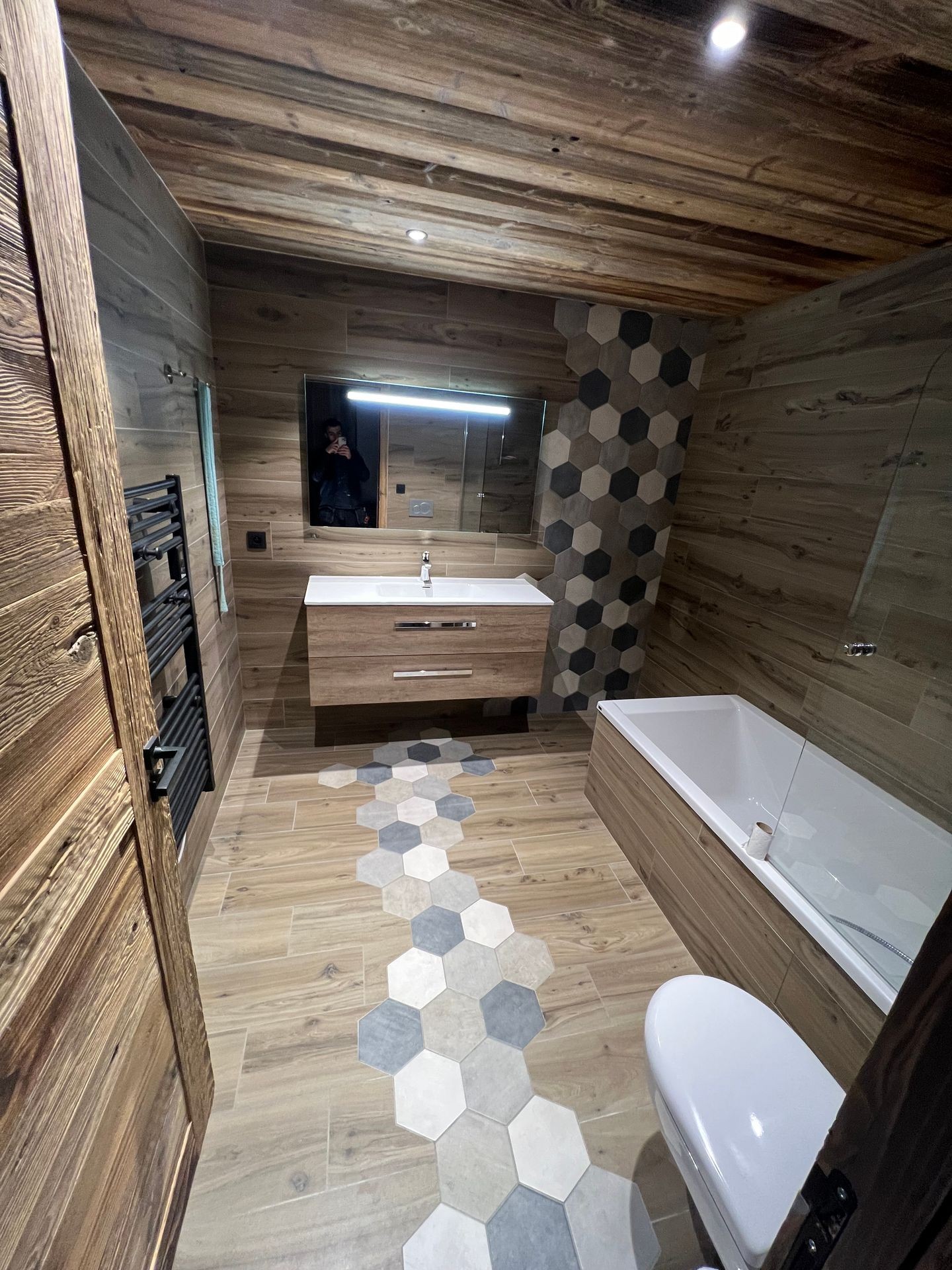 Modern bathroom with wooden accents, hexagonal tiles, and a large mirror above the sink.