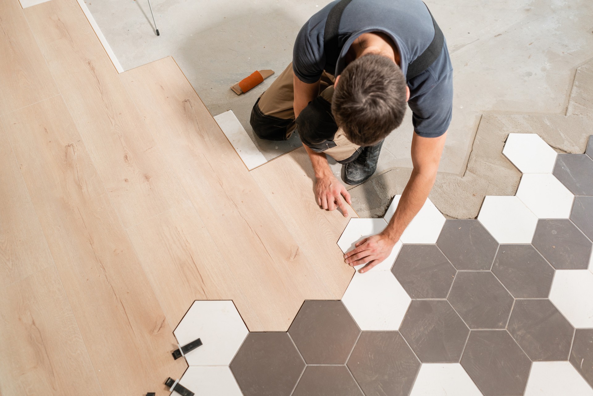 Travailleur de sexe masculin installation nouveau parquet stratifié. La combinaison de panneaux de stratifié et céramique carreaux en forme de nid d’abeilles. Rénovation de la cuisine.